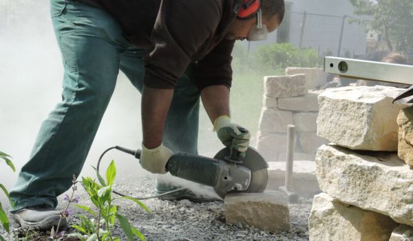 Mann sägt Stein für Trockenmauer im neuen Wildbienenschaugarten in Berlin-Treptow.